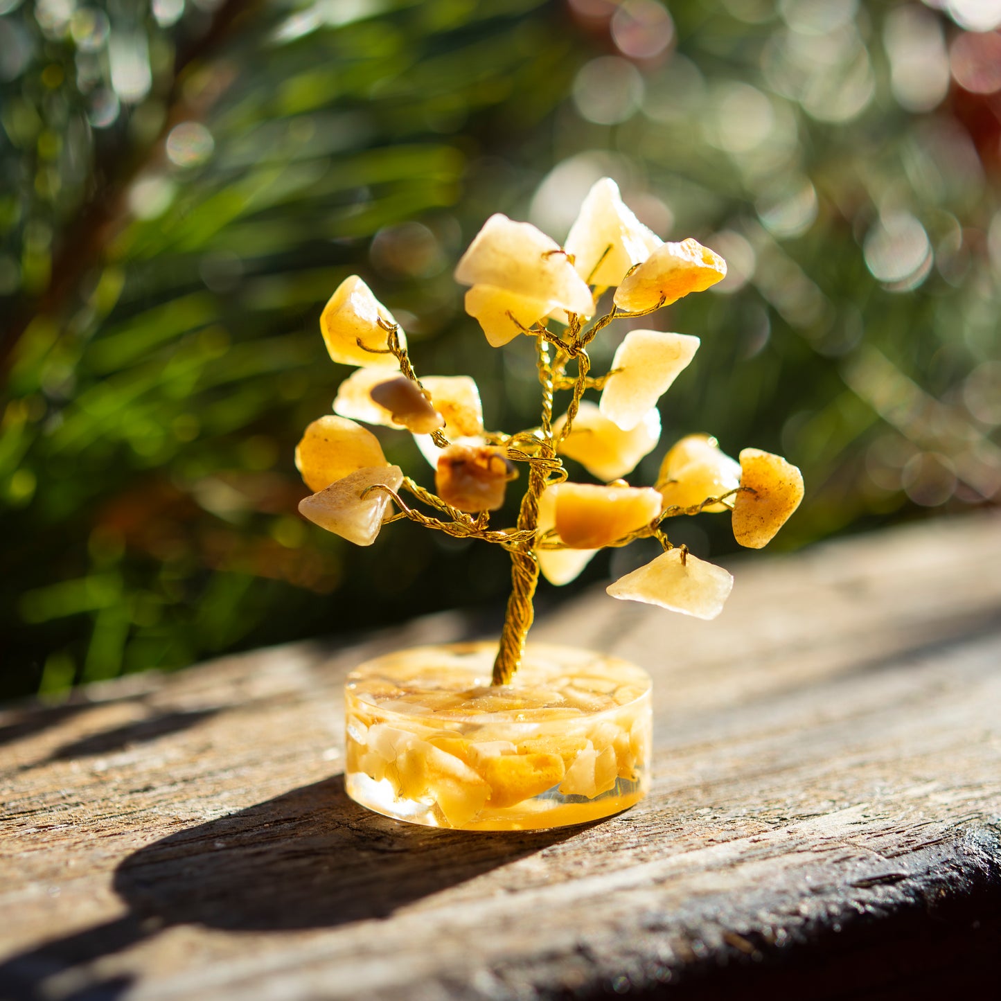Dekoratives Bäumchen aus Limonit-Steinen mit goldfarbenem Draht auf einer sonnigen Holzoberfläche, umgeben von unscharfem, grünem Hintergrund.