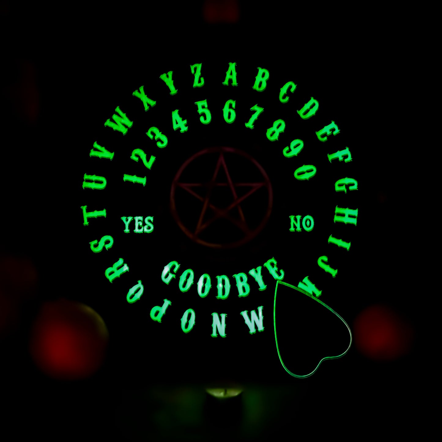 Ein Ouija-Brett, das im Dunkeln leuchtet, mit leuchtenden Buchstaben von A bis Z und Zahlen von 0 bis 9. In der Mitte befindet sich ein Pentagramm, umgeben von den Worten ‘YES’ und ‘NO’. Unten stehen die Wörter ‘GOODBYE’. Das Brett wird durch ein mystisches grünes Leuchten hervorgehoben.