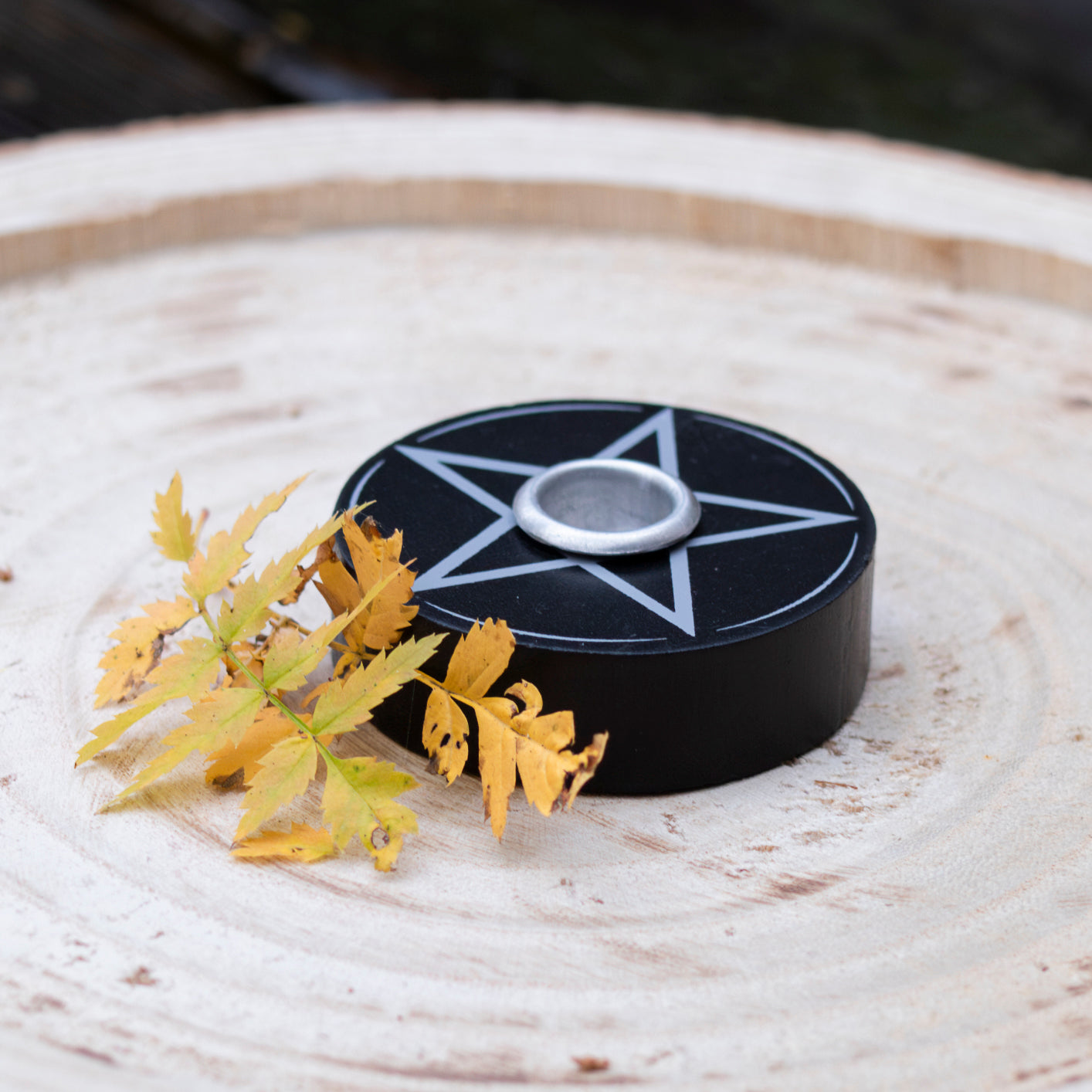 Pentagramm-Kerzenhalter dekorativ auf einer Holzscheibe platziert und mit Herbstblättern verziert.