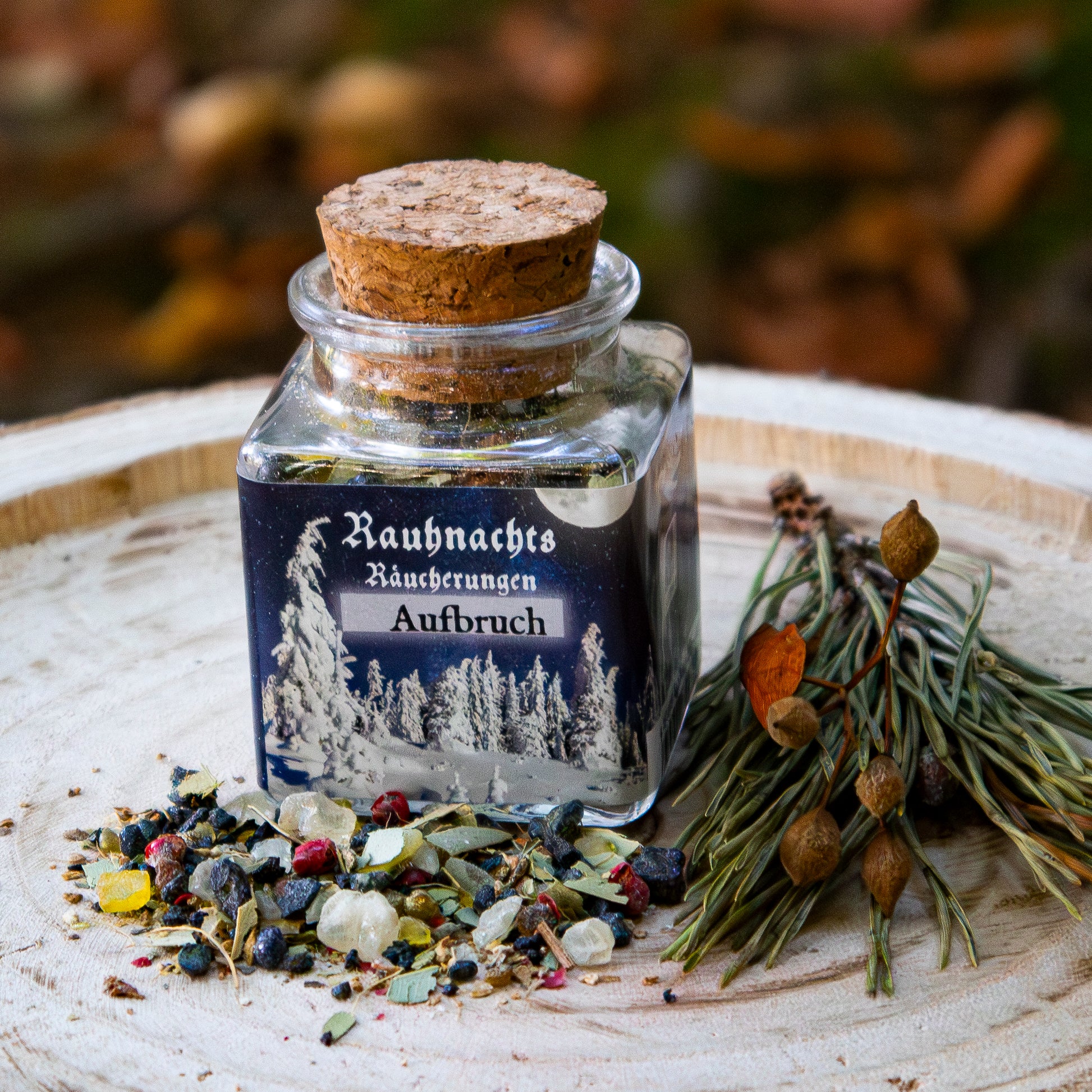 Ein Glas mit Korkverschluss, beschriftet mit ‘Rauhnachts Räucherungen Aufbruch’, gefüllt mit Harzen und Kräutern. Das Glas steht auf einer Holzscheibe, umgeben von verstreuten Harzen, Beeren und dekorativen getrockneten Zweigen vor einem natürlichen Hintergrund.