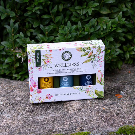 Ein Wellness-Set mit ätherischen Ölen in einer dekorativen Verpackung mit floralen Mustern, platziert auf einer Steinfläche vor einer Hecke.