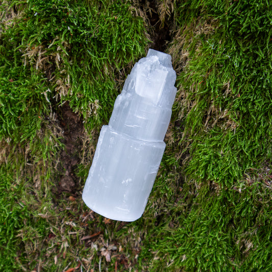 Ein klarer, transparenter Selenit-Kristall in Form eines “Eisbergs”, der auf einem weichen, natürlichen Hintergrund aus grünem Moos liegt.