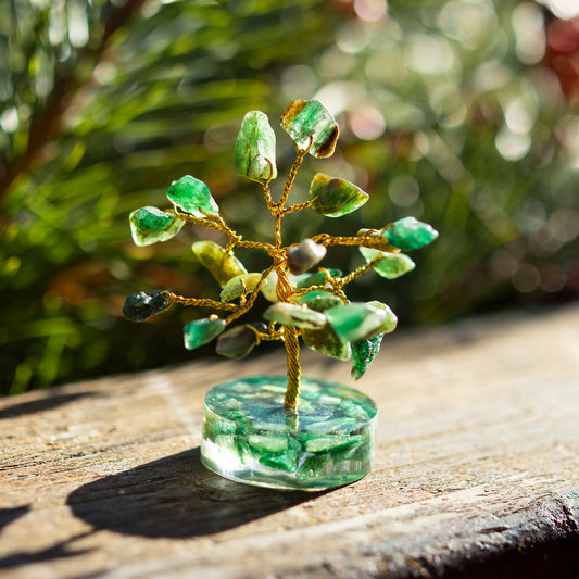 Dekoratives Bäumchen aus Aventurin-Steinen mit goldfarbenem Draht auf einer sonnigen Holzoberfläche, umgeben von unscharfem, grünem Hintergrund.