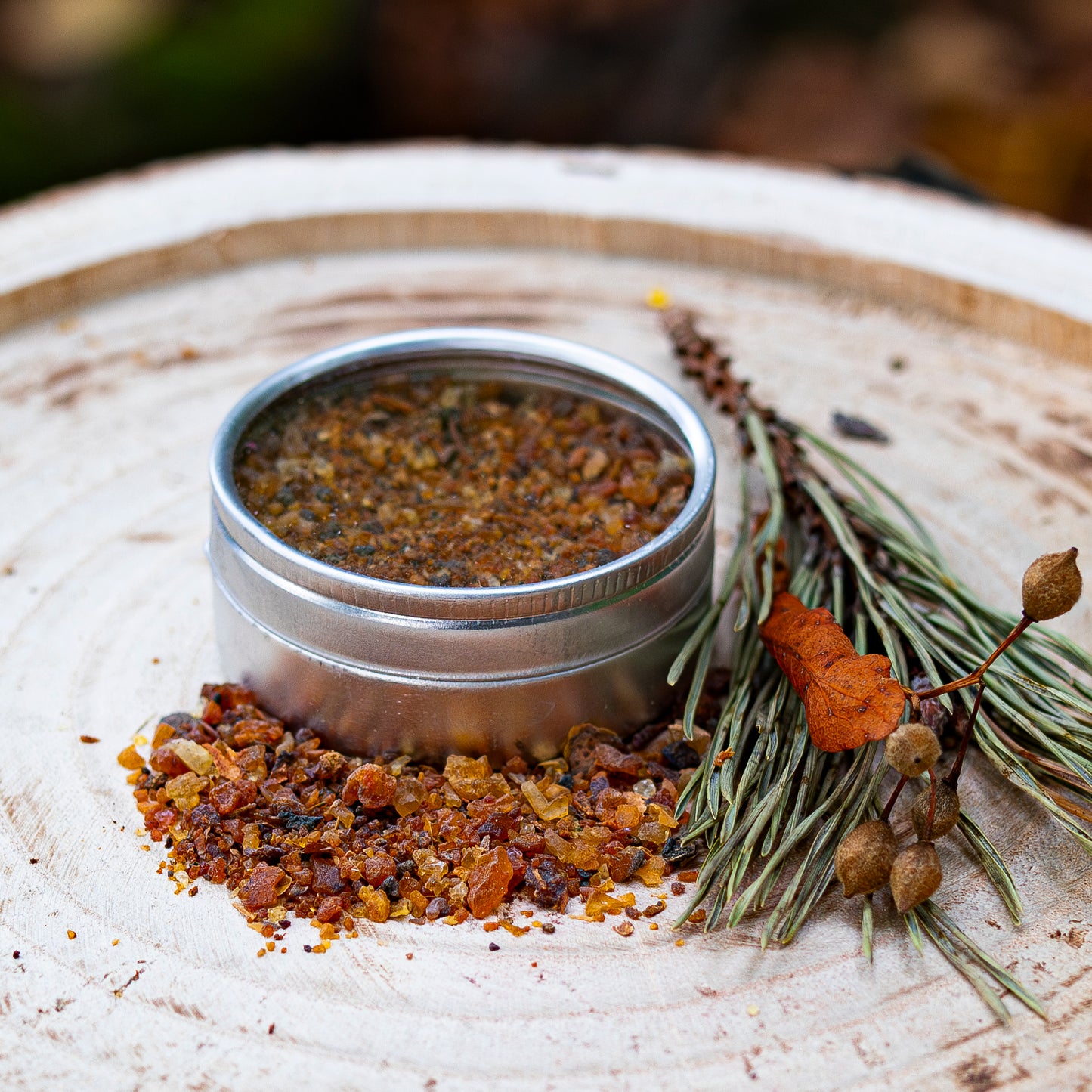 Silberne Dose mit geöffnetem Deckel, gefüllt mit Myrrhe-Harz, dekorativ mit verstreuten Harzstücken und einem kleinen Tannenzweig-Bündel auf einer Holzscheibe präsentiert.