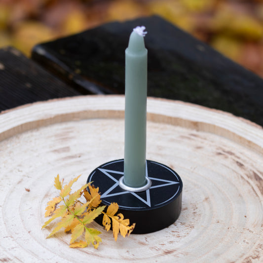 Pentagramm-Kerzenhalter mit einer grünen Kerze, dekorativ auf einer Holzscheibe platziert und mit Herbstblättern verziert.