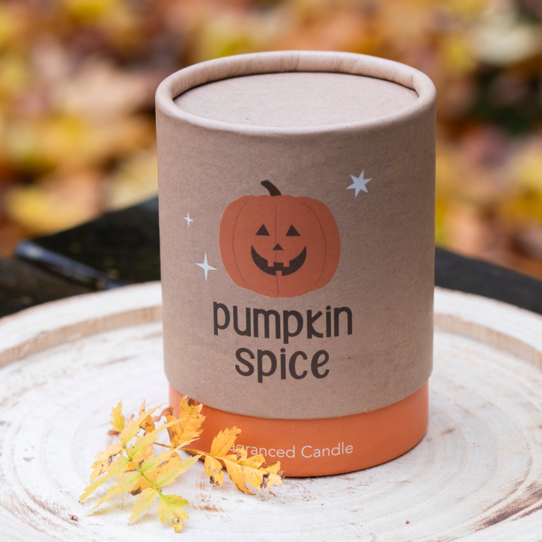 Eine stilvolle Verpackung mit dem Aufdruck ‘Pumpkin Spice’ und einer niedlichen Kürbisgrafik. Der warme braune Farbton und die schlichte Typografie vermitteln eine herbstliche Atmosphäre. Die Verpackung ist auf einer hellen Holzscheibe platziert, dekoriert mit herbstlichen Blättern, die eine gemütliche, saisonale Stimmung schaffen.