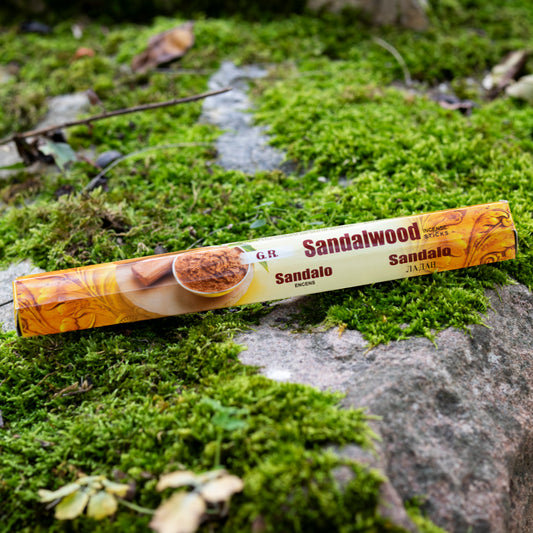 Verpackung von Sandelholz-Räucherstäbchen in warmen Braun- und Beigetönen, dekorativ auf einem moosbedeckten Stein in einer natürlichen Umgebung arrangiert.