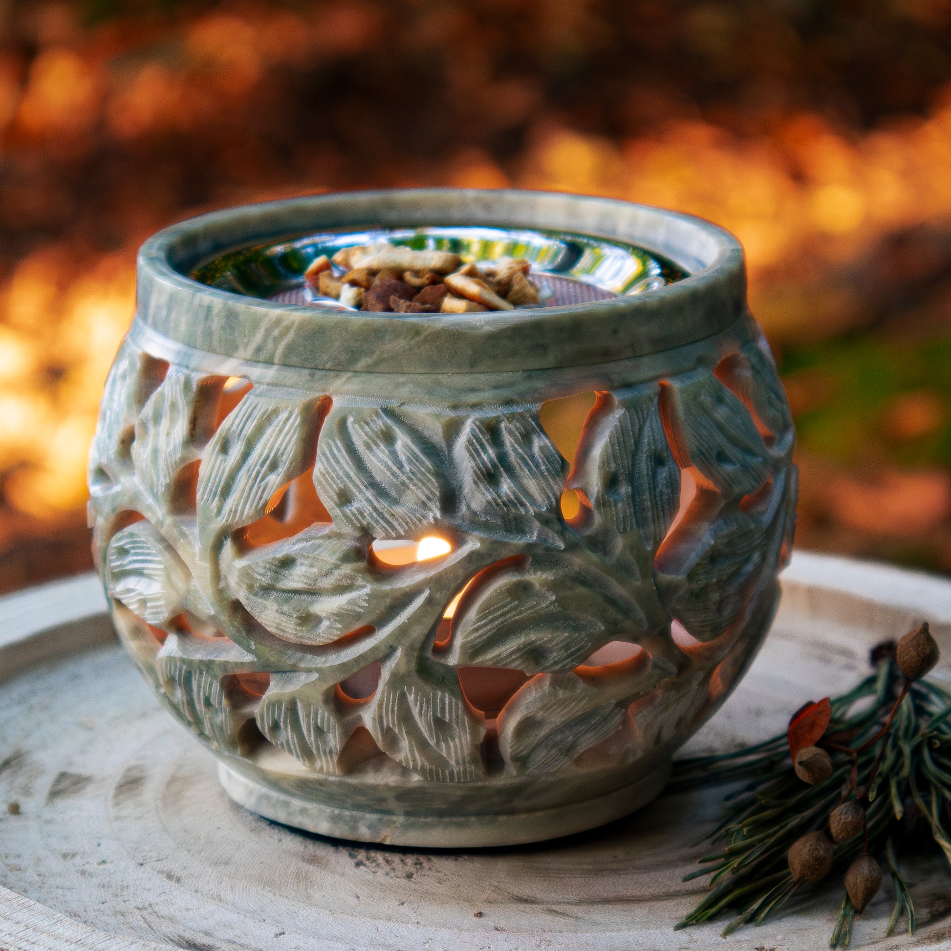 Beigefarbener Specksteinhalter mit floralem Design, auf einer Holzscheibe präsentiert, dekoriert mit einem natürlichen Zweig im Hintergrund.